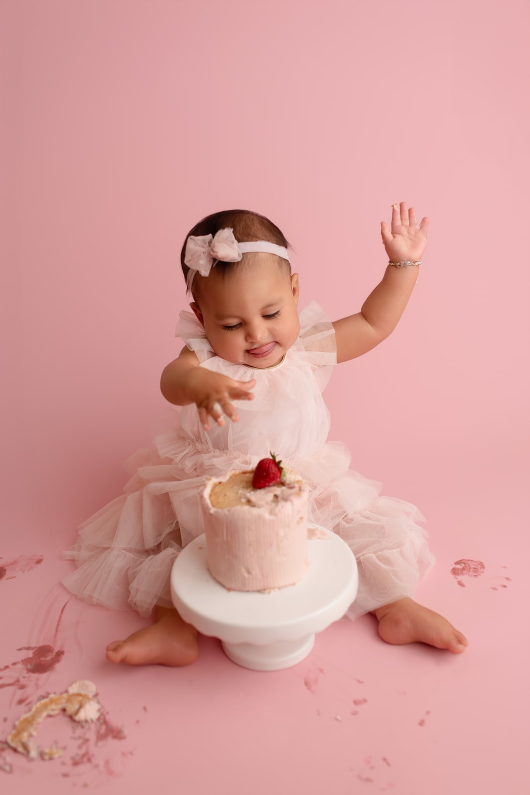 Toddler in pink tulle reaching for cake at a smash session
