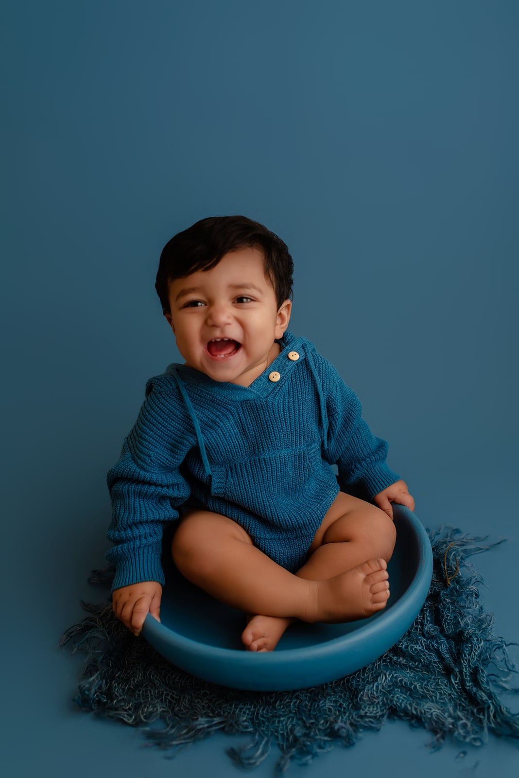 Baby sitting in a blue bowl prop against a blue backdrop