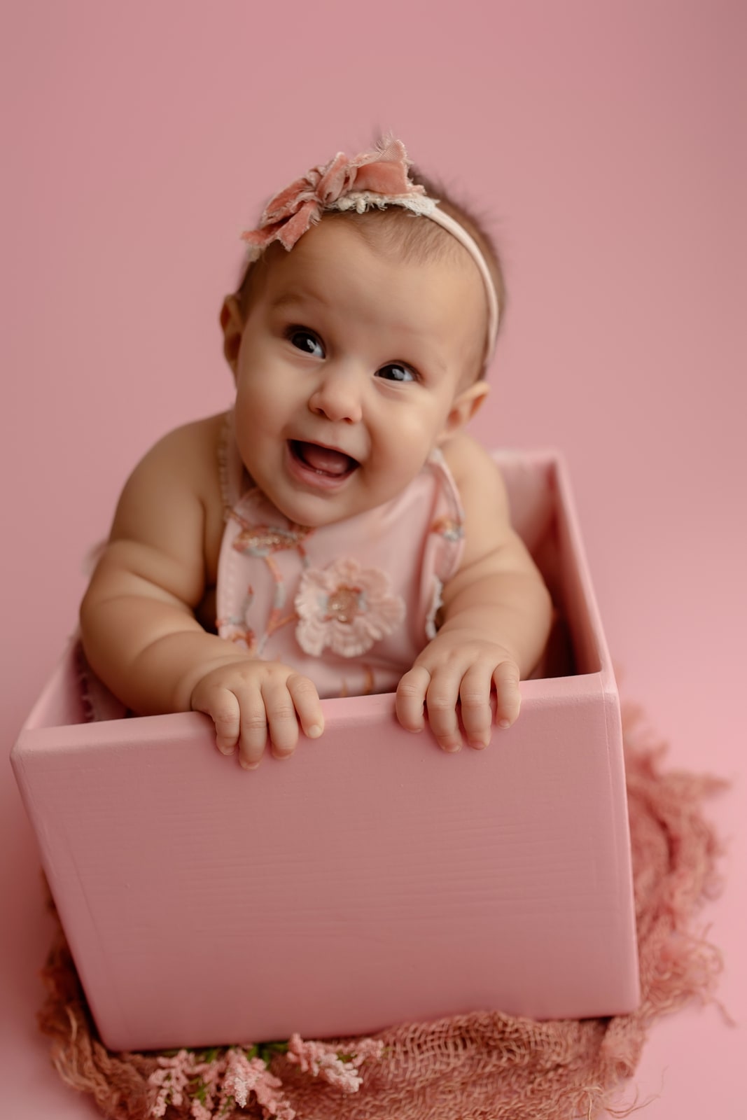 Baby in a floral outfit sitting in a pink box