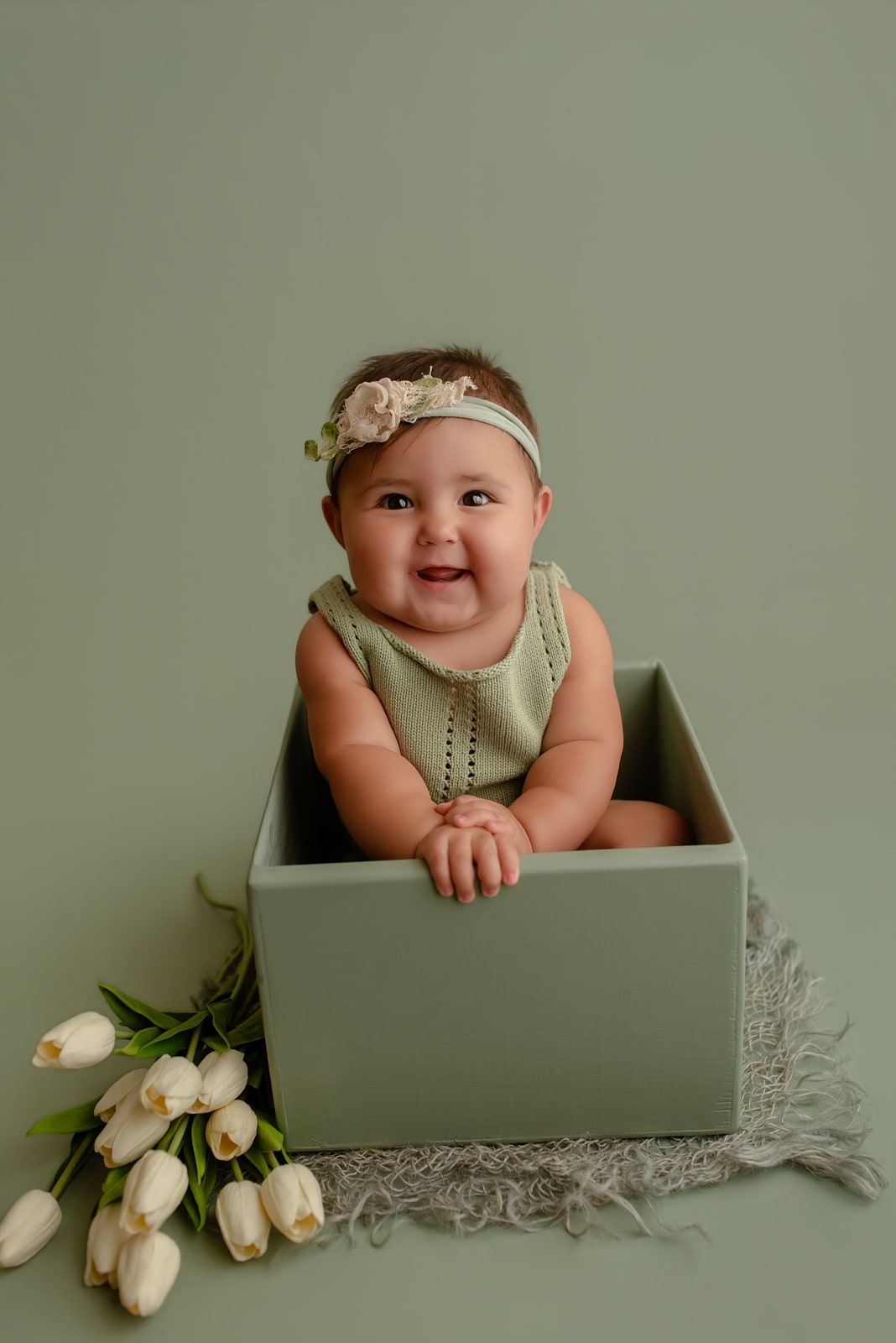 Baby sitting in a sage green box with white tulips